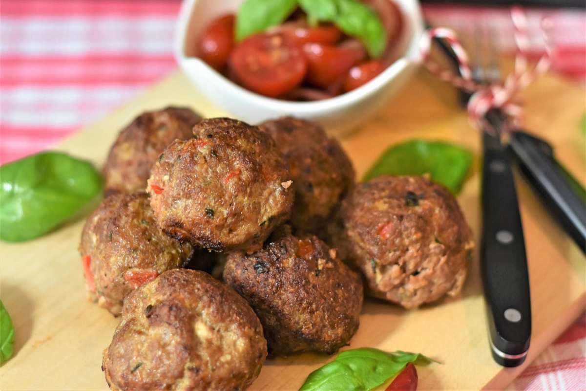 polpette con accanto le posate e una ciotola di pomodorini