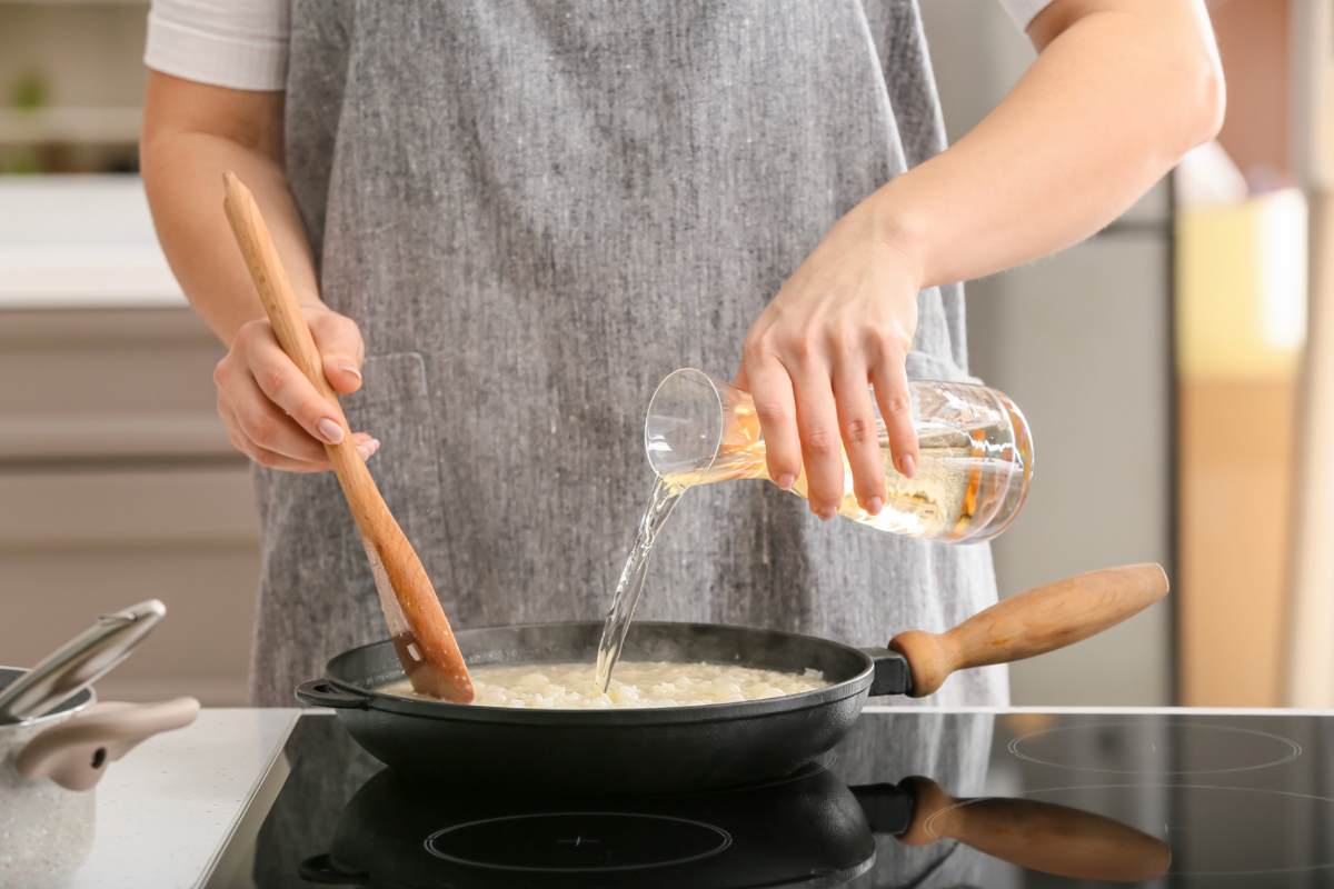 Donna che versa acqua nella padella con risotto