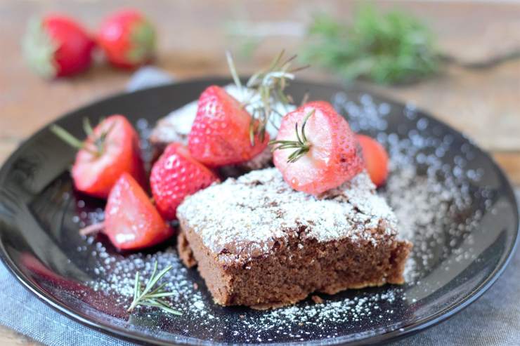 fetta di torta al cacao con zucchero a velo e fragole in un piatto