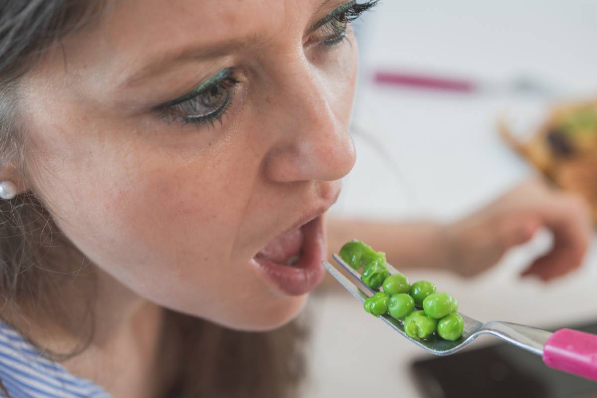 Donna che mangia una forchettata di piselli