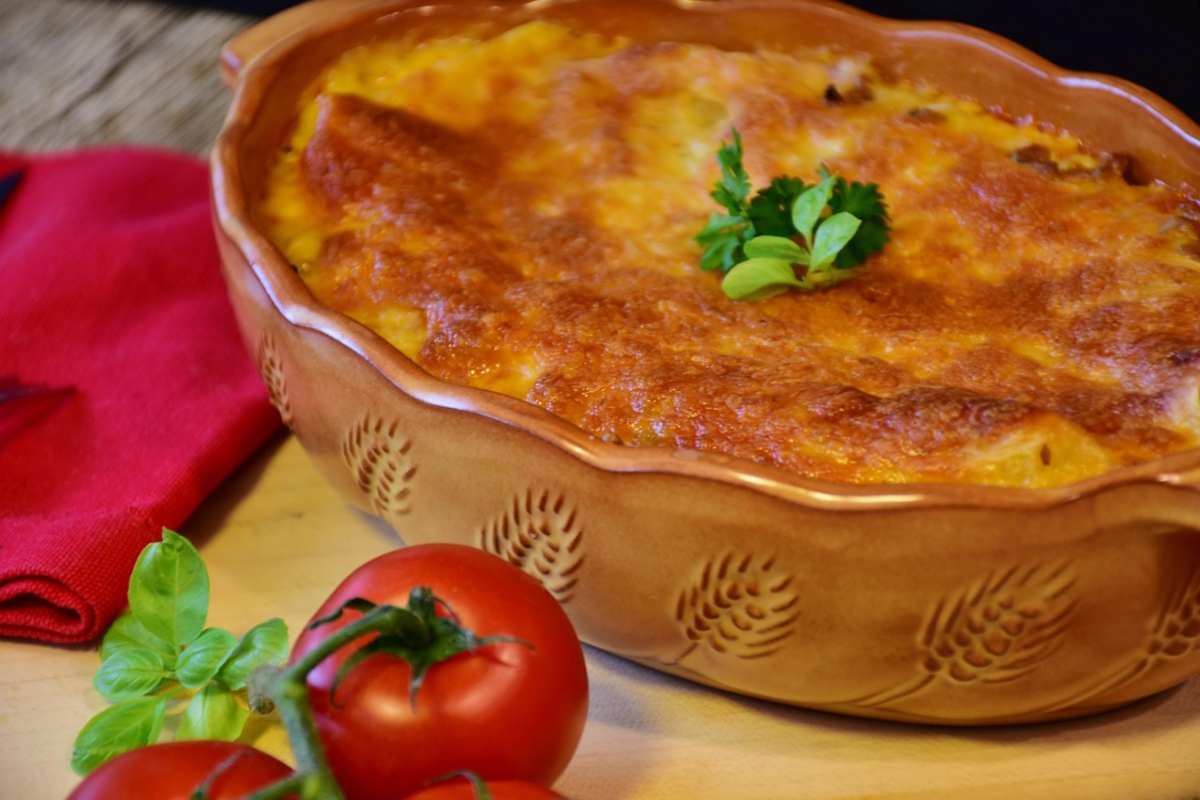 teglia di lasagna con accanto pomodori e foglioline di menta