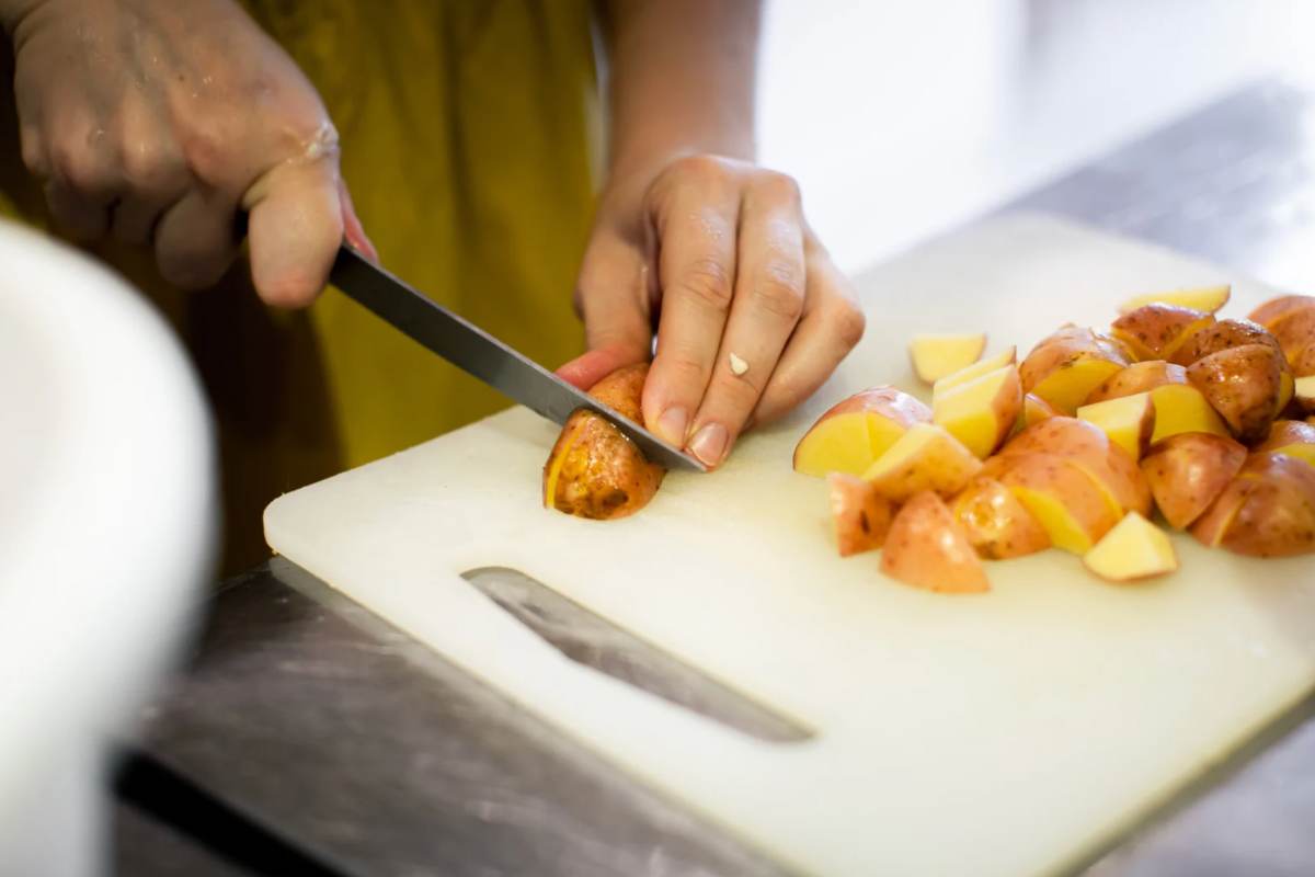 Persona che taglia le patate su un tagliere in plastica